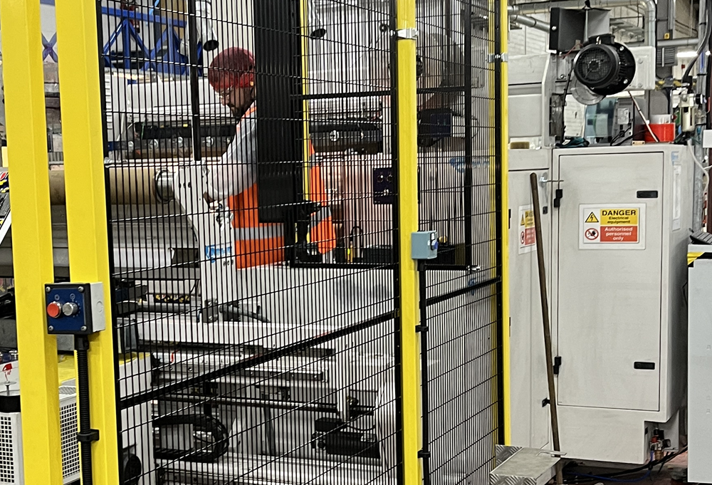 Factory worker operating a machine behind a fixed guard.