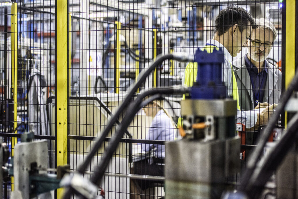 image of Three engineers in a factory working behind a fence. Machine in the foreground for the Compliance services page