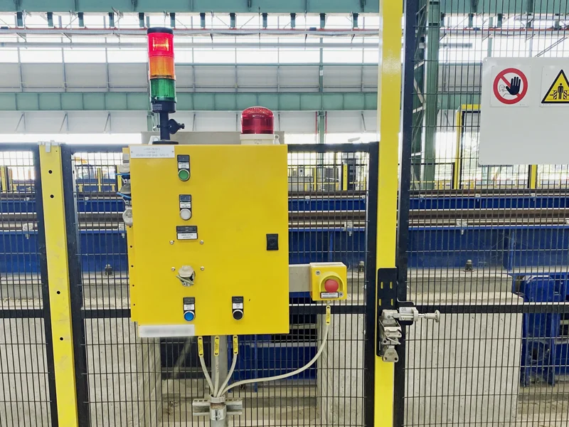 A Fortress Safety control panel featuring a trapped key interlock, push buttons, and an emergency stop, mounted next to a safety gate with signal tower lights above.