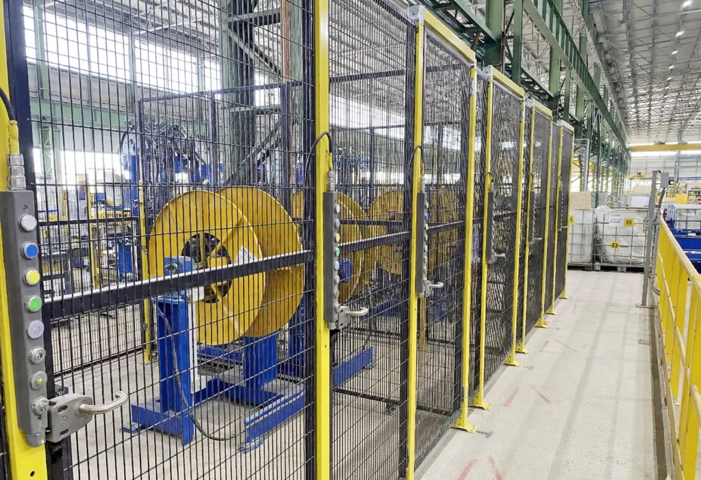 A series of safety gates in a steel plant equipped with Fortress tGard interlocks, featuring integrated controls and handles, securing a line of heavy machinery.