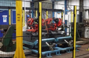 Robotic welding cell enclosed by perimeter fencing within plant-wide safety architecture in heavy industrial facility